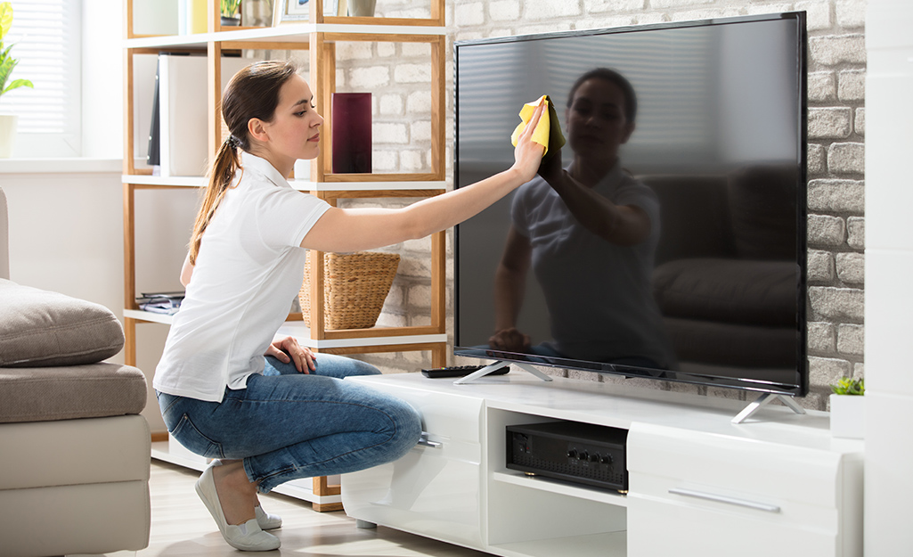 A person wiping a flat screen television with a microfiber cloth.