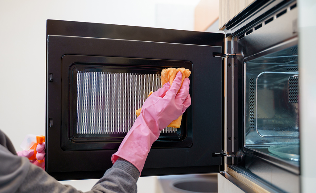 A person wipes the interior of a microwave oven.
