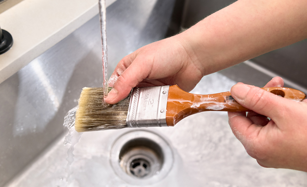 Person washing paint brush in a sink with water.