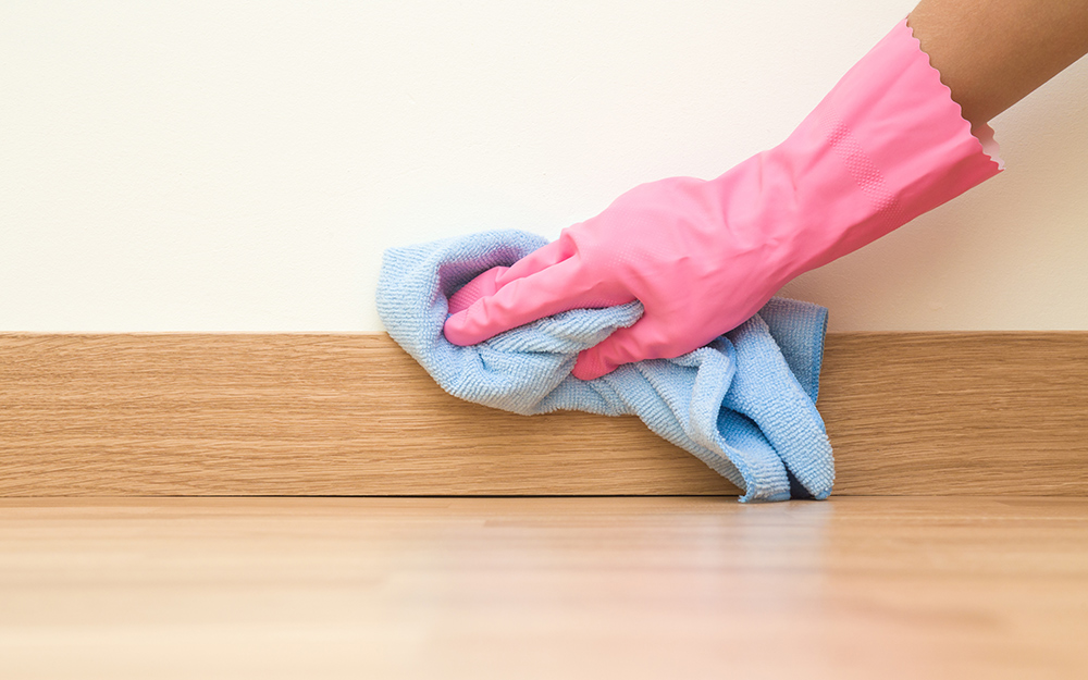 A person wipes a baseboard with a cloth.