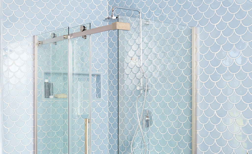 A shower stall with blue tile and clear, clean glass doors