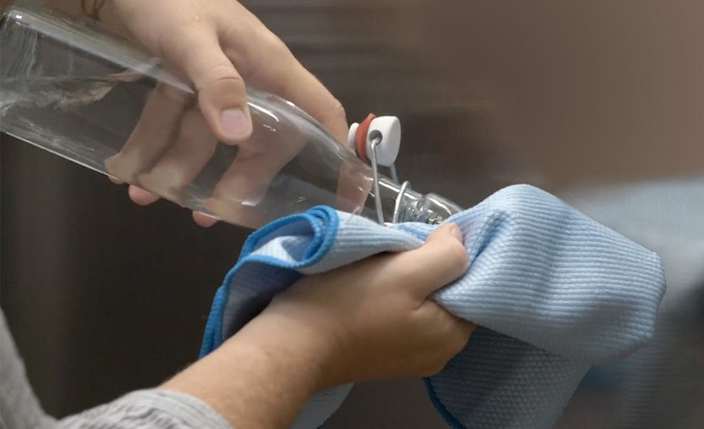 Person adding vinegar to a cloth in front of a stainless steel refrigerator.