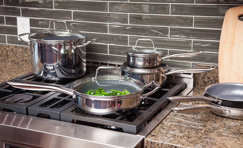 Shiny stainless steel cookware sits on a stove and countertop.