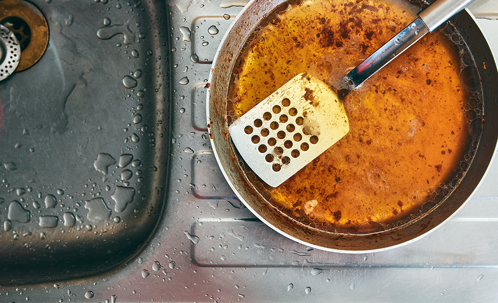 A dirty stainless steel pan and spatula sit next to a sink.