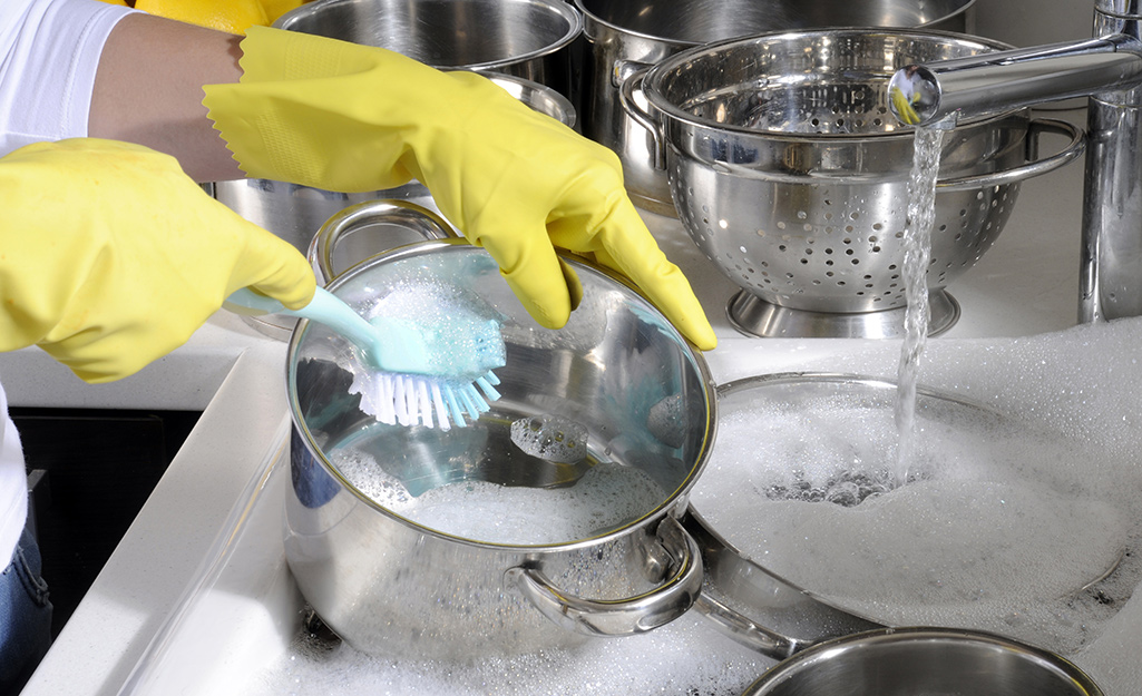 Someone washes a sink full of stainless steel cookware that's soaking in soapy water.