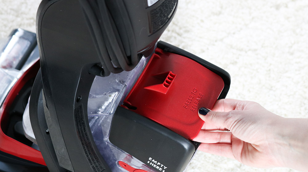 A person removes the water chamber from a Hoover carpet cleaner.