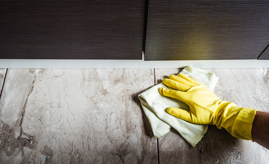 A person wearing kitchen gloves to clean a ceramic tile floor.