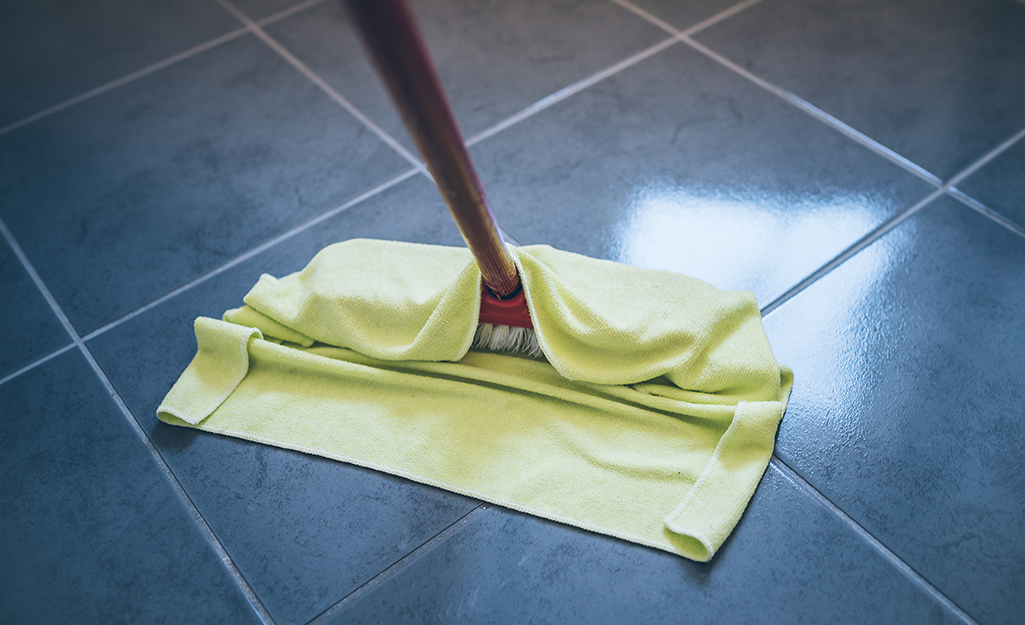 A person using a flat mop to clean a natural stone tile floor.