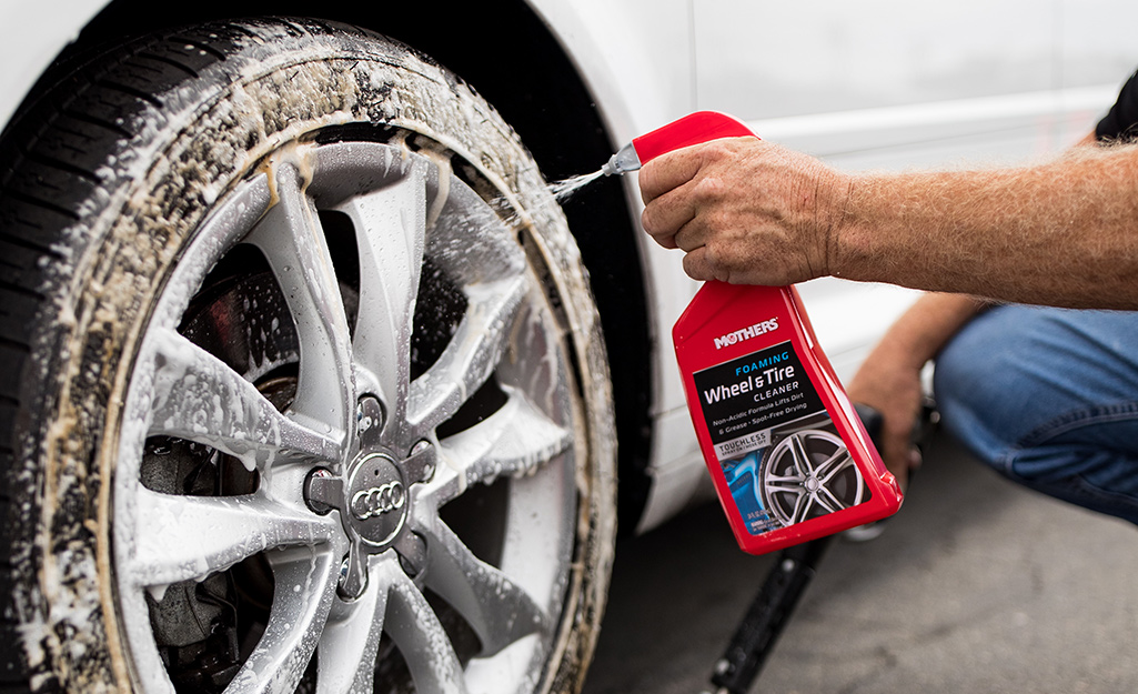 A person sprays tire cleaner onto the tire of a car.