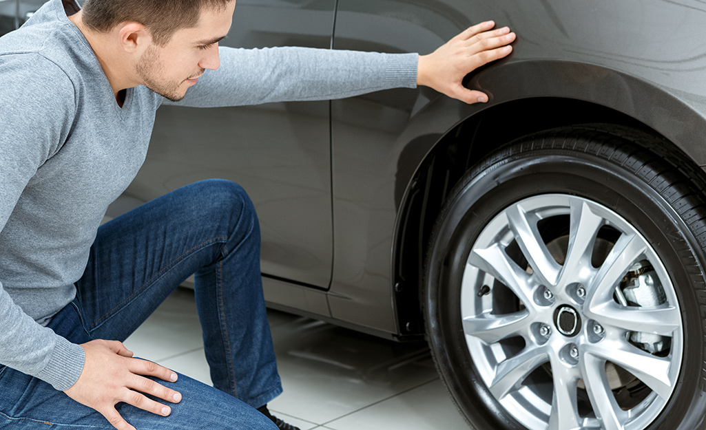 A man examines one of the tires on a car.