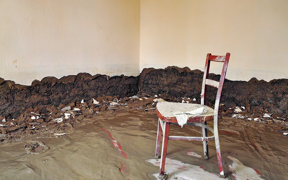 A wood chair sits on a mud-covered floor after a flood.