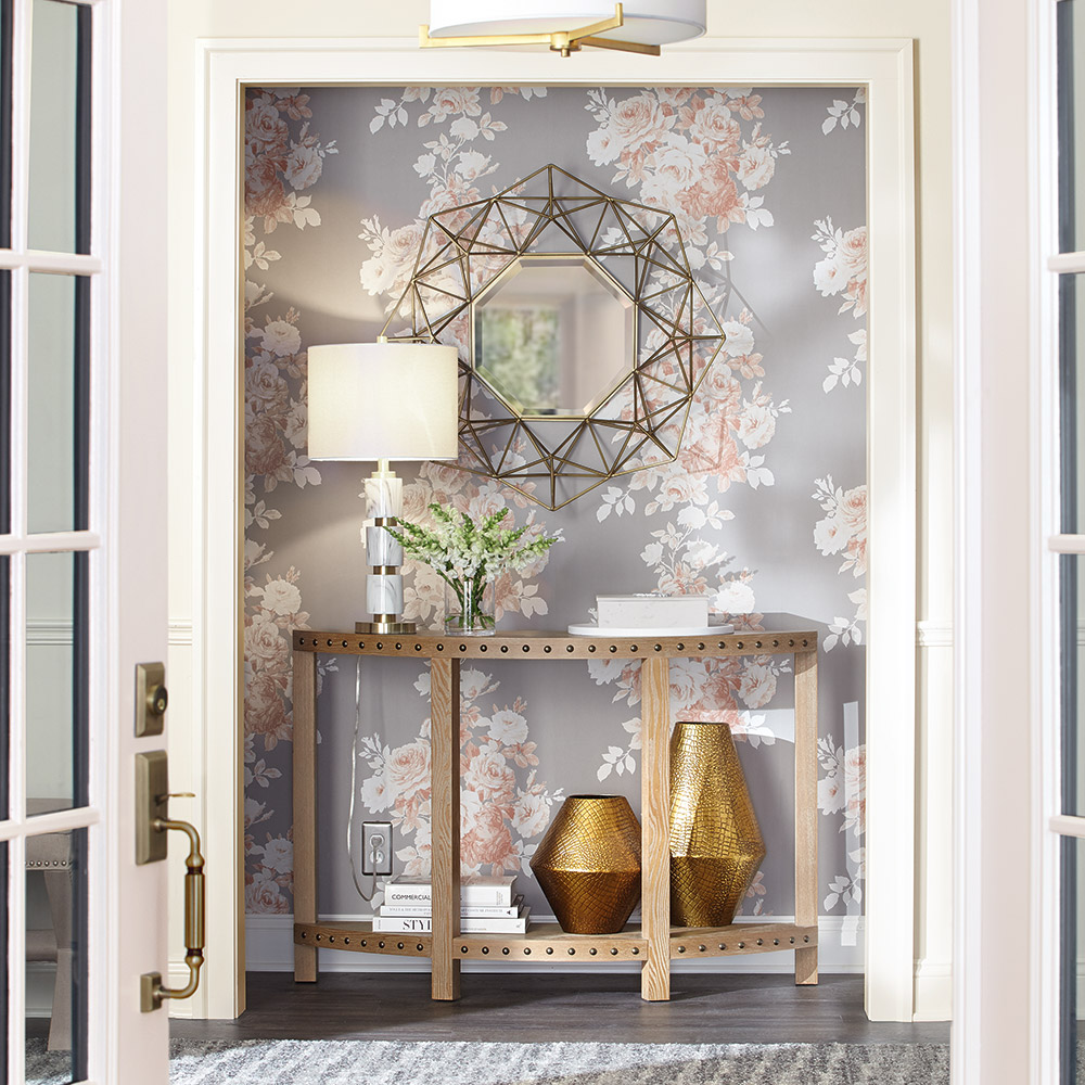 Gray and blush floral wallpaper hangs behind a gold table in an entranceway.