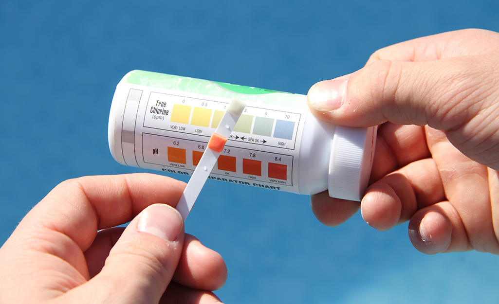 A person compares a pool test strip to the results color chart on the side of the test strip bottle.