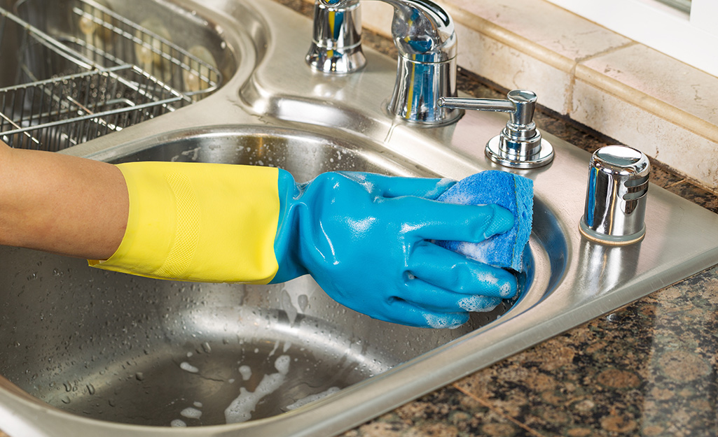 Someone wearing gloves and cleaning kitchen sink.