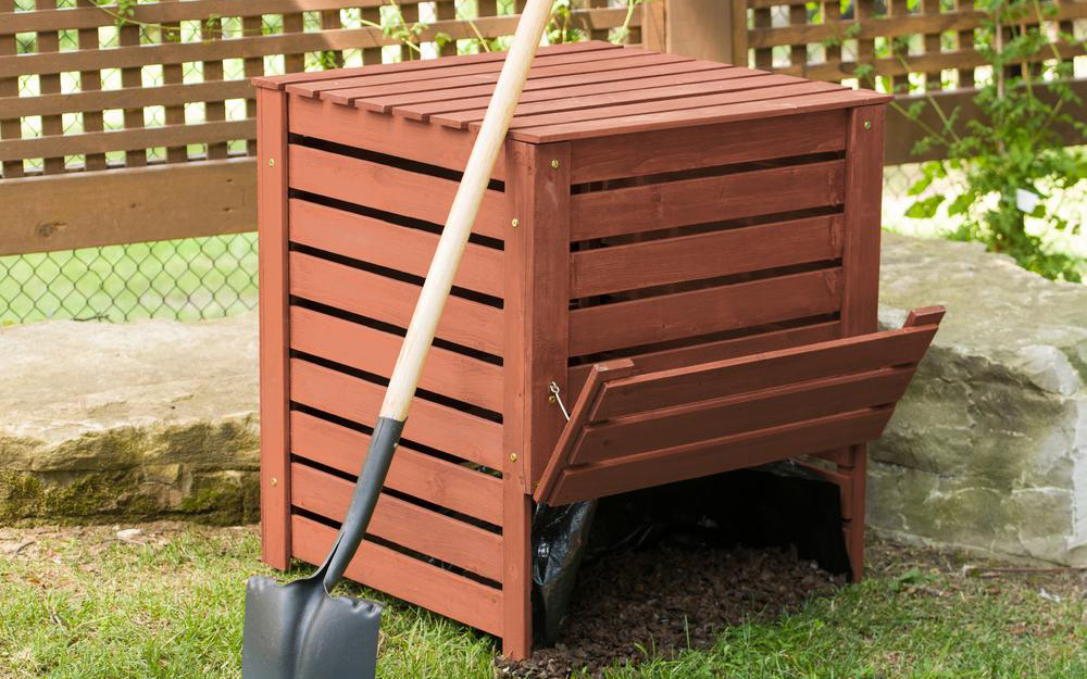 a wooden composter in a yard with a shovel leaning against it a wooden composter in a yard with a shovel leaning against it