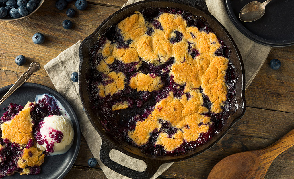 Smoked blackberry cobbler in a cast iron with a plate serving next to it with ice cream.