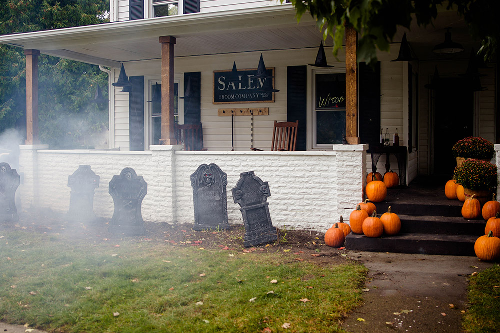 A white home decorated for Halloween with pumpkins, tombstones, and floating witch hats.