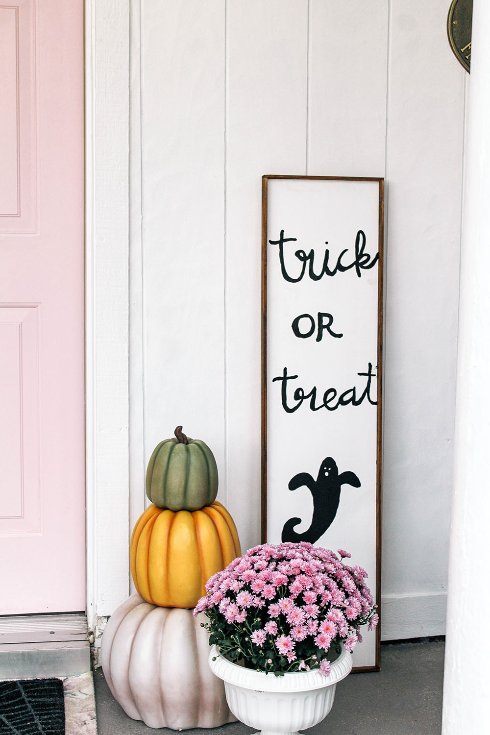 A trick or treat sign standing next to a trio of stacked pumpkins. A trick or treat sign standing next to a trio of stacked pumpkins.