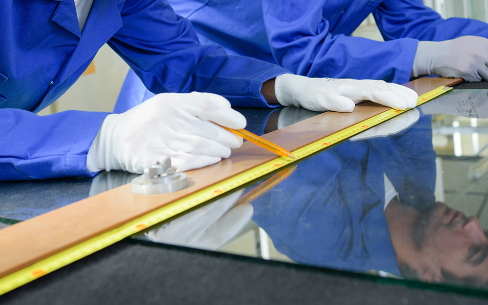 a person using a ruler and marker to measure and mark a sheet of glass