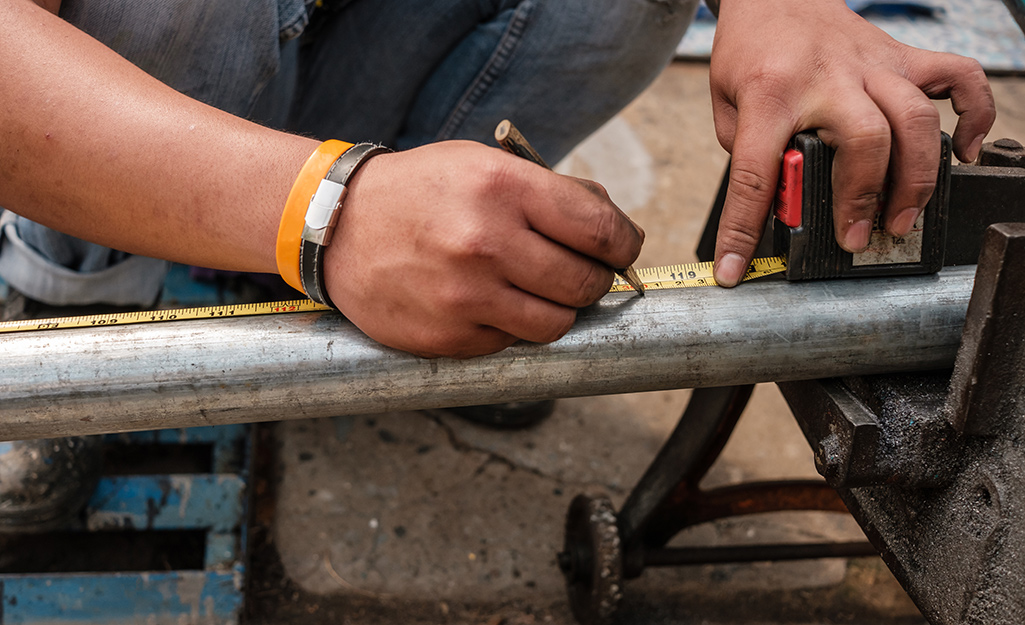 A person makes a mark on a length of steel pipe with the help of a tape measure.