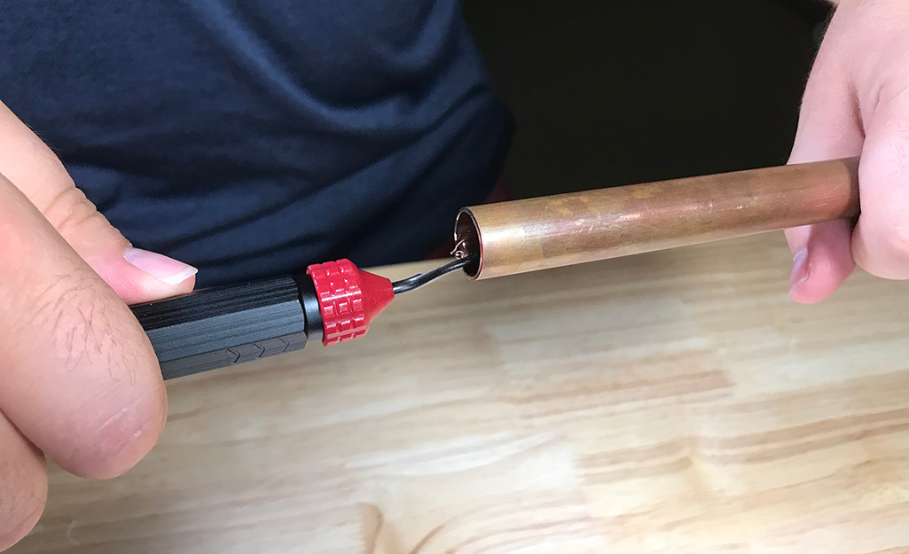 A person uses a deburring tool on the end of copper pipe.