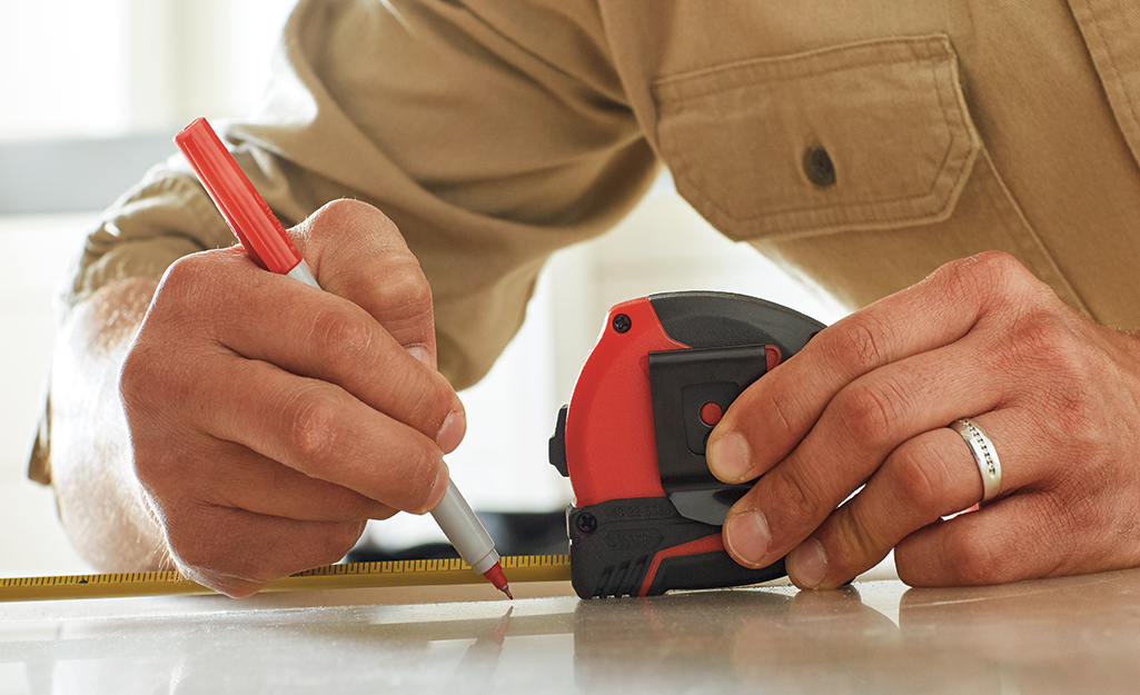 Person marking measurements on a sheet of plexiglass with a red pen.