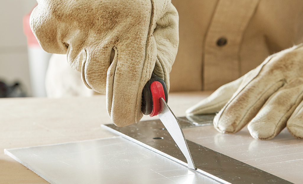 Person scoring plexiglass along the edge of a metal ruler.