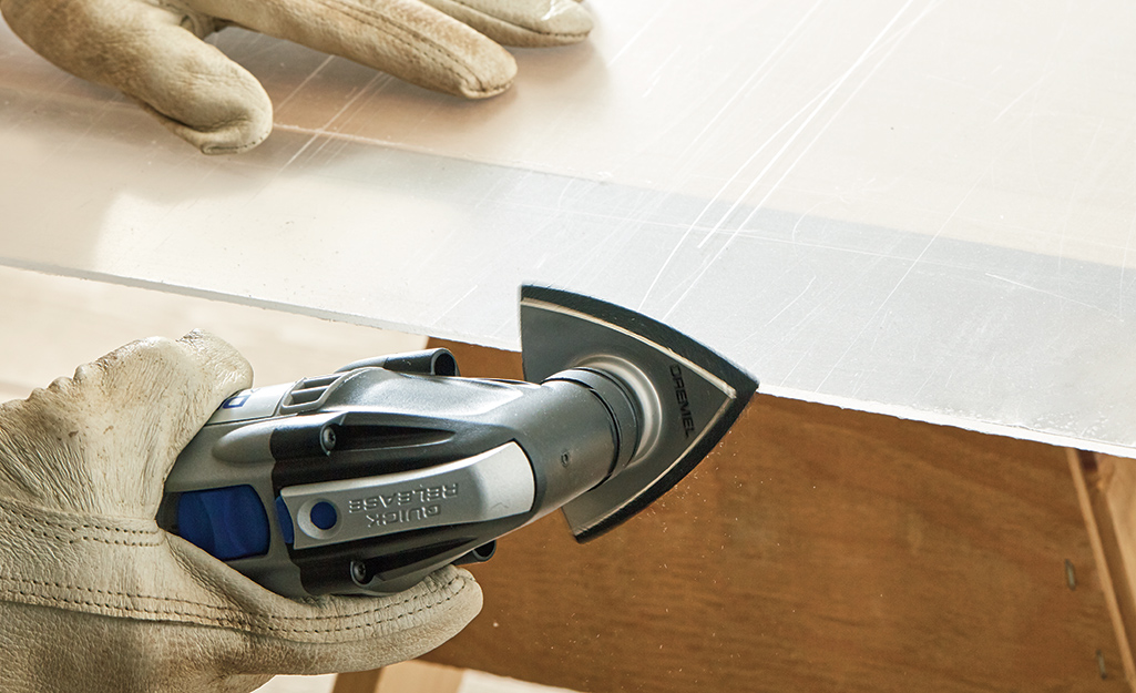 A man using a hand-held sander on the edge of a piece of plexiglass.