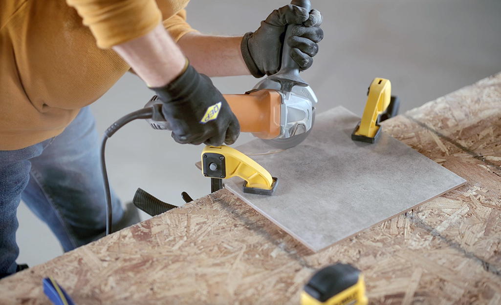 A person uses an angle grinder to cut a piece of tile.