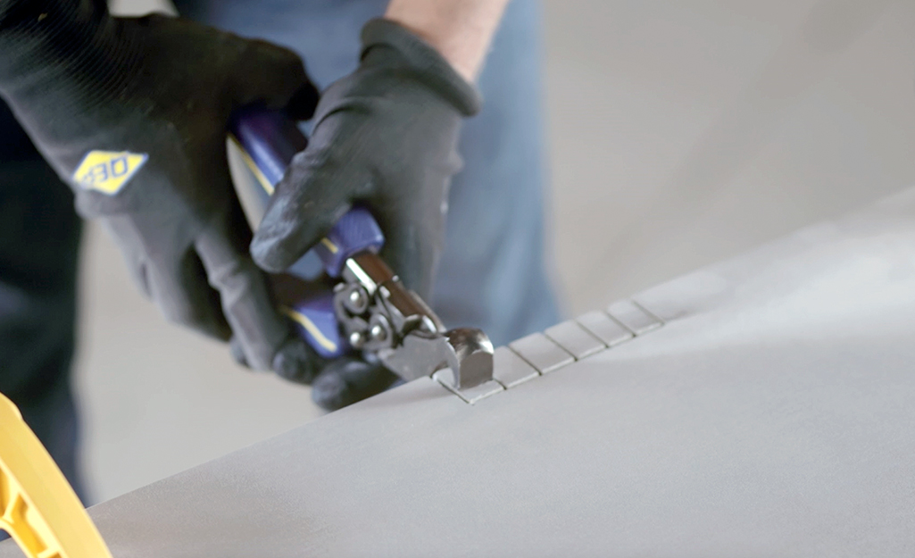 A person using tile nippers to complete a notch cut on a piece of tile.