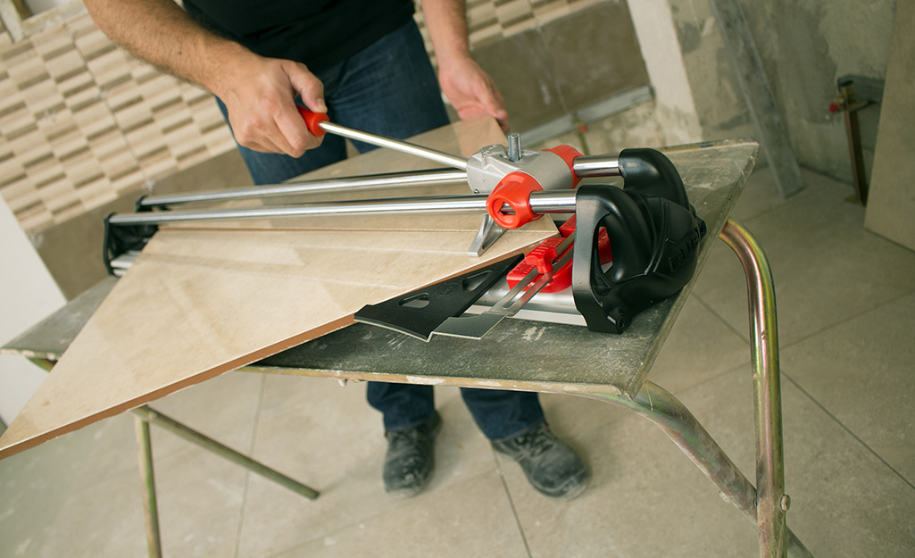 A person uses a manual tile cutter to cut a piece of tile.