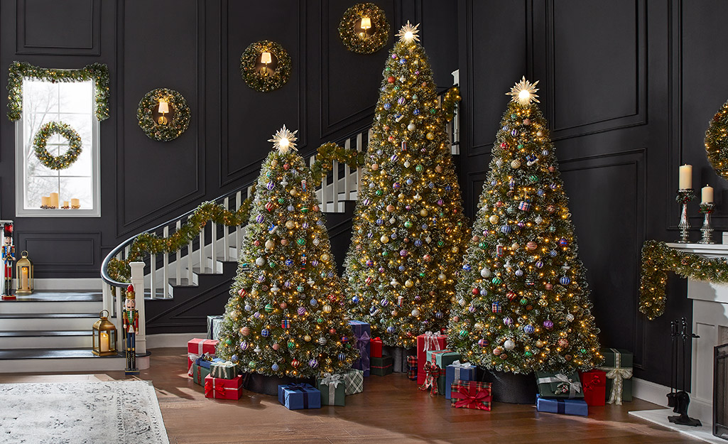 Three lighted Christmas trees by a decorated staircase