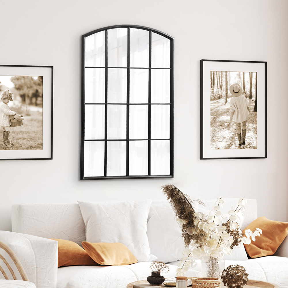 A large decorative mirror hangs over a white sofa in a living room between two pieces of wall art.