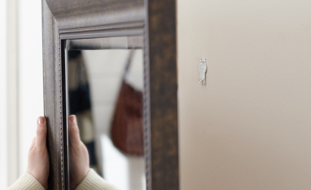 Someone hanging a mirror on a wall with a hook. Someone hanging a mirror on a wall with a hook.
