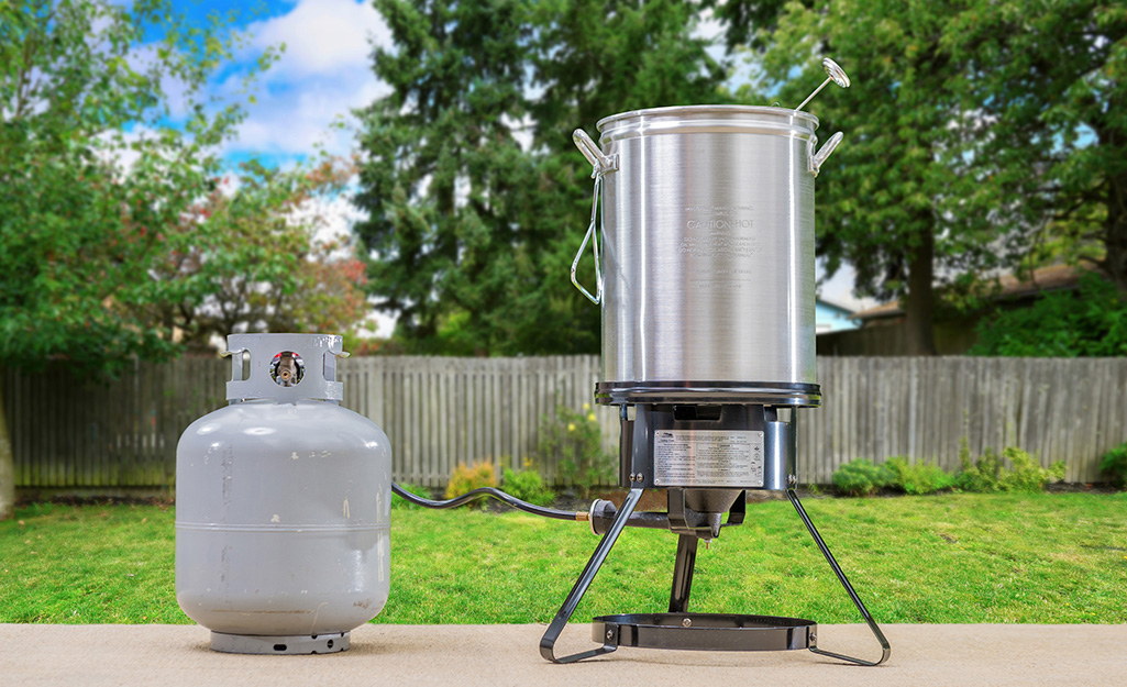 A turkey fryer and propane tank stand on a patio.