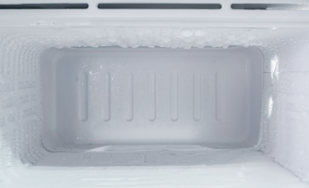 Open freezer door revealing melting ice layer. Open freezer door revealing melting ice layer.