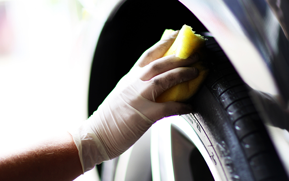 A person cleans a car tire with a sponge.