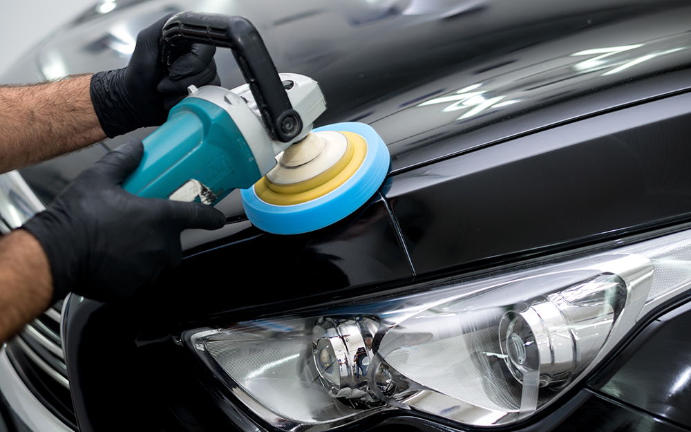 A person uses a power polisher on the exterior paint of a car.