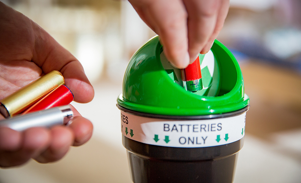 A person puts batteries into a small recycling container.