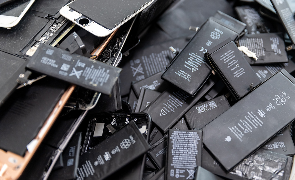Laptop batteries, cell phone batteries and old phones are piled on top of each other.
