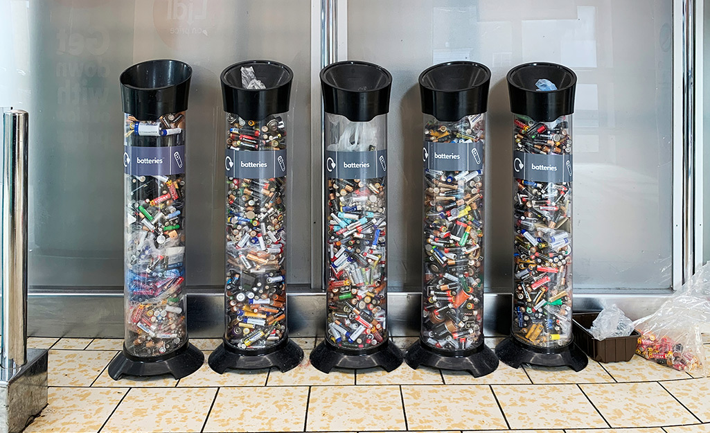 Five large cylindrical containers for recycling batteries stand side by side.