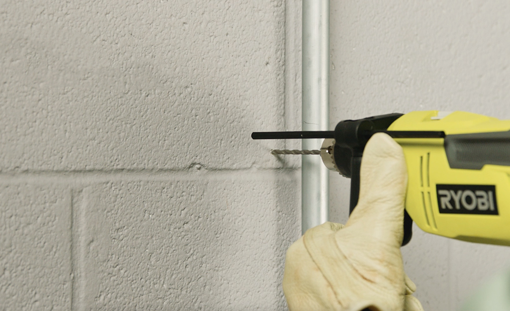 A person using a drill on concrete wall. 