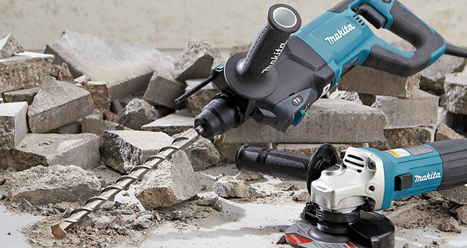 A hammer drill resting on the ground with pieces of broken concrete.