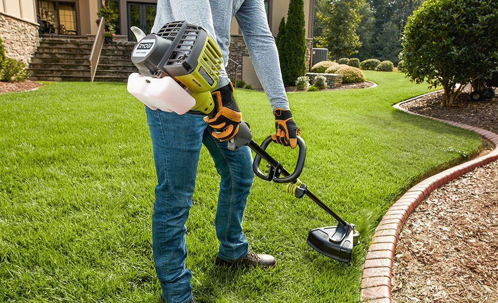 A person using a gas string trimmer along a mulched bed. 