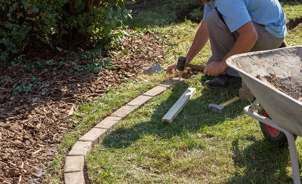 A person making a curved paver border near trees.