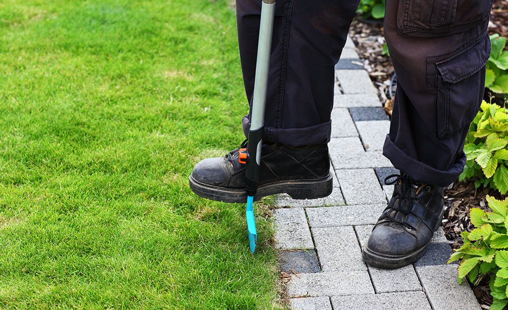 A person using a manual edger along a brick border.