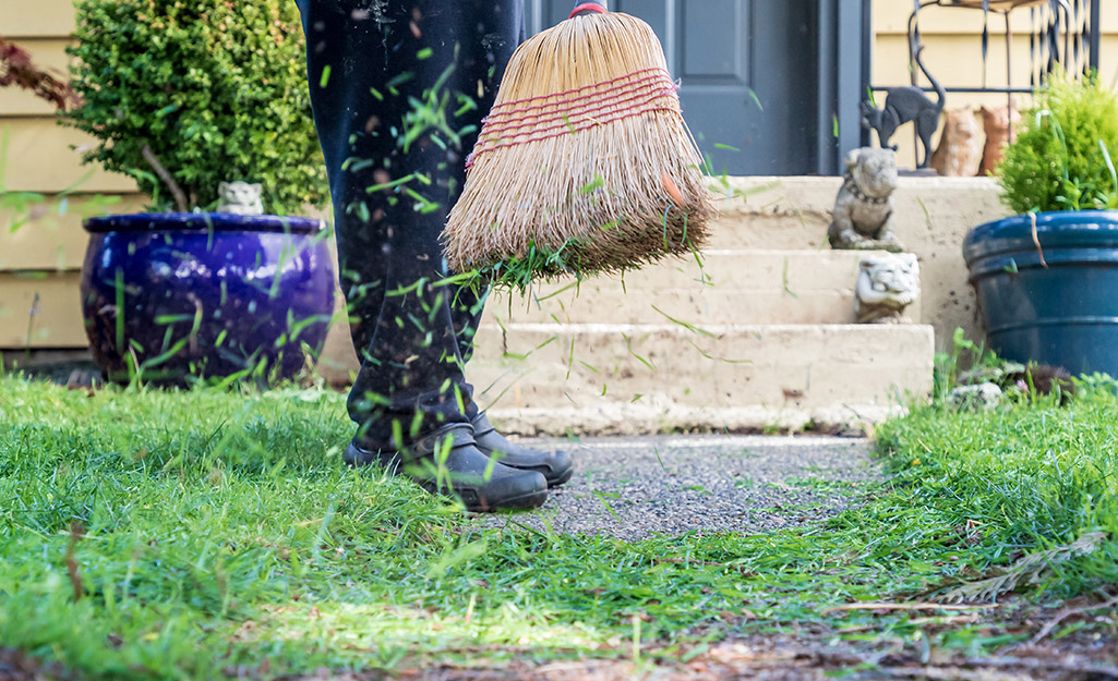 A person sweeping up grass clippings along a sidewalk.