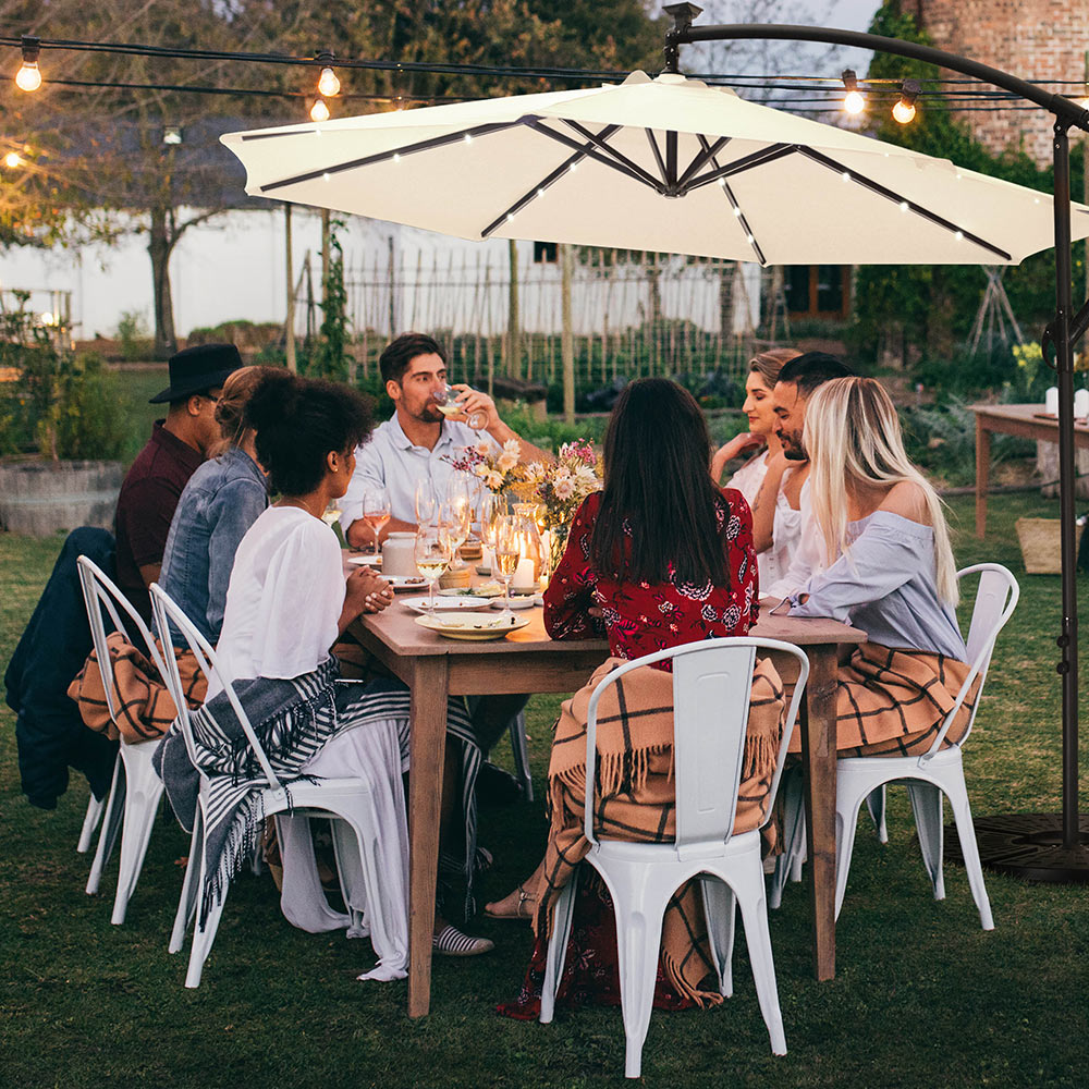 A group of people has a meal around an outdoor table with a patio umbrella.