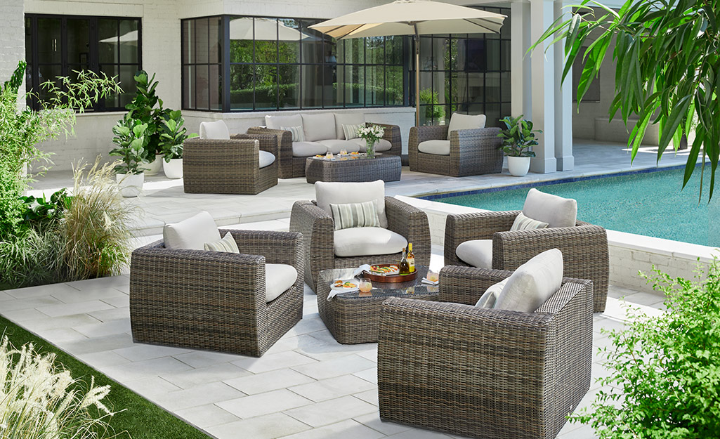 Four outdoor chairs sit on a patio next a swimming pool.