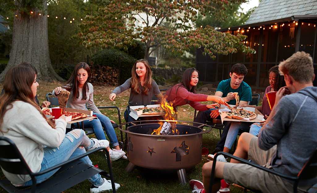 A group of people eats pizza while sitting around a fire pit.